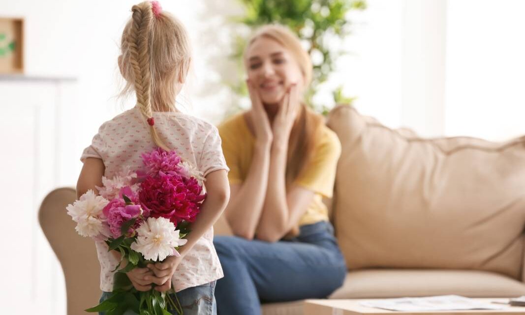 little girl holding flowers behind her back for her mum