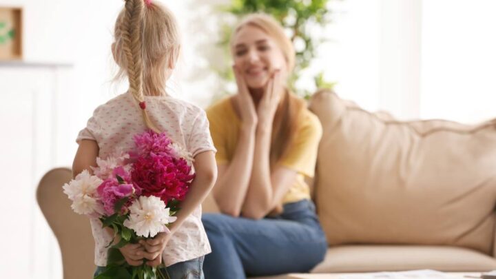 little girl holding flowers behind her back for her mum